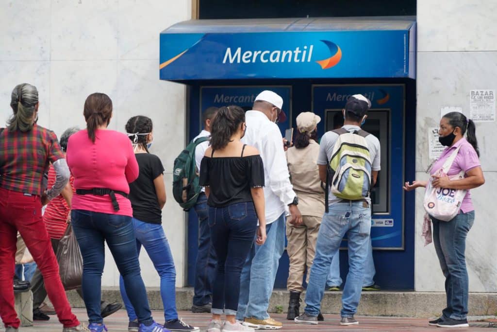 Personas con tapabocas haciendo cola para retirar efectivo de un cajero del Banco Mercantil