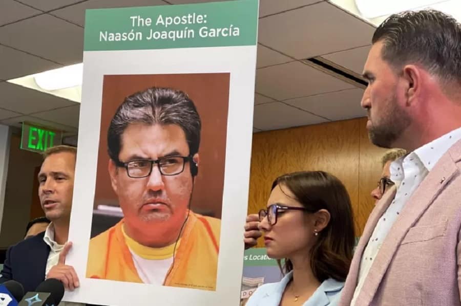 El abogado Mike Rick sostiene un cartel con la cara de Naason Joaquin Garcia junto a Sochil Martin y Sharim Guzman.